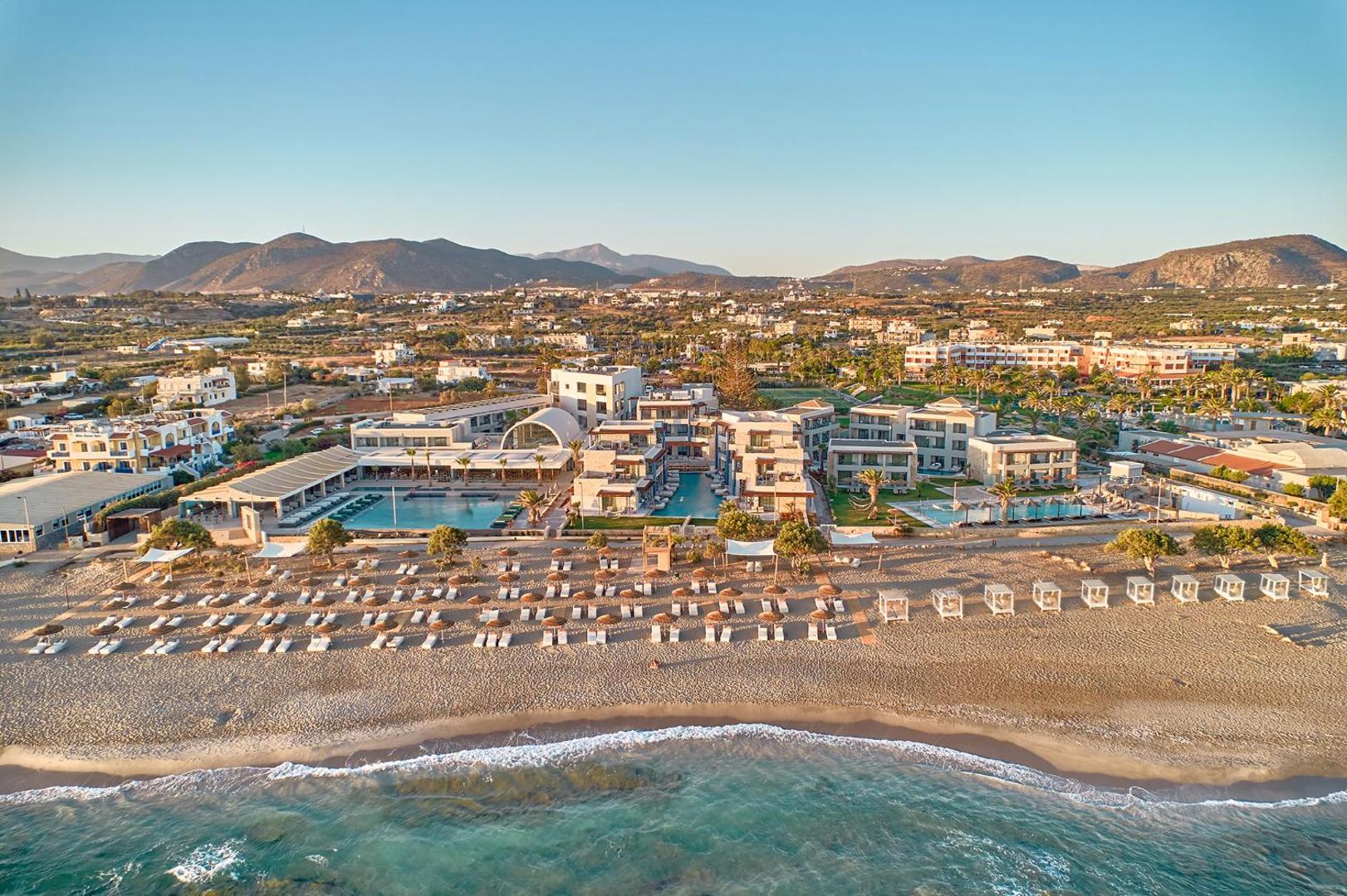 Panorāmas skats uz Paralos Kosta Alímia viesnīcu, smilšu pludmali un kalniem fonā.