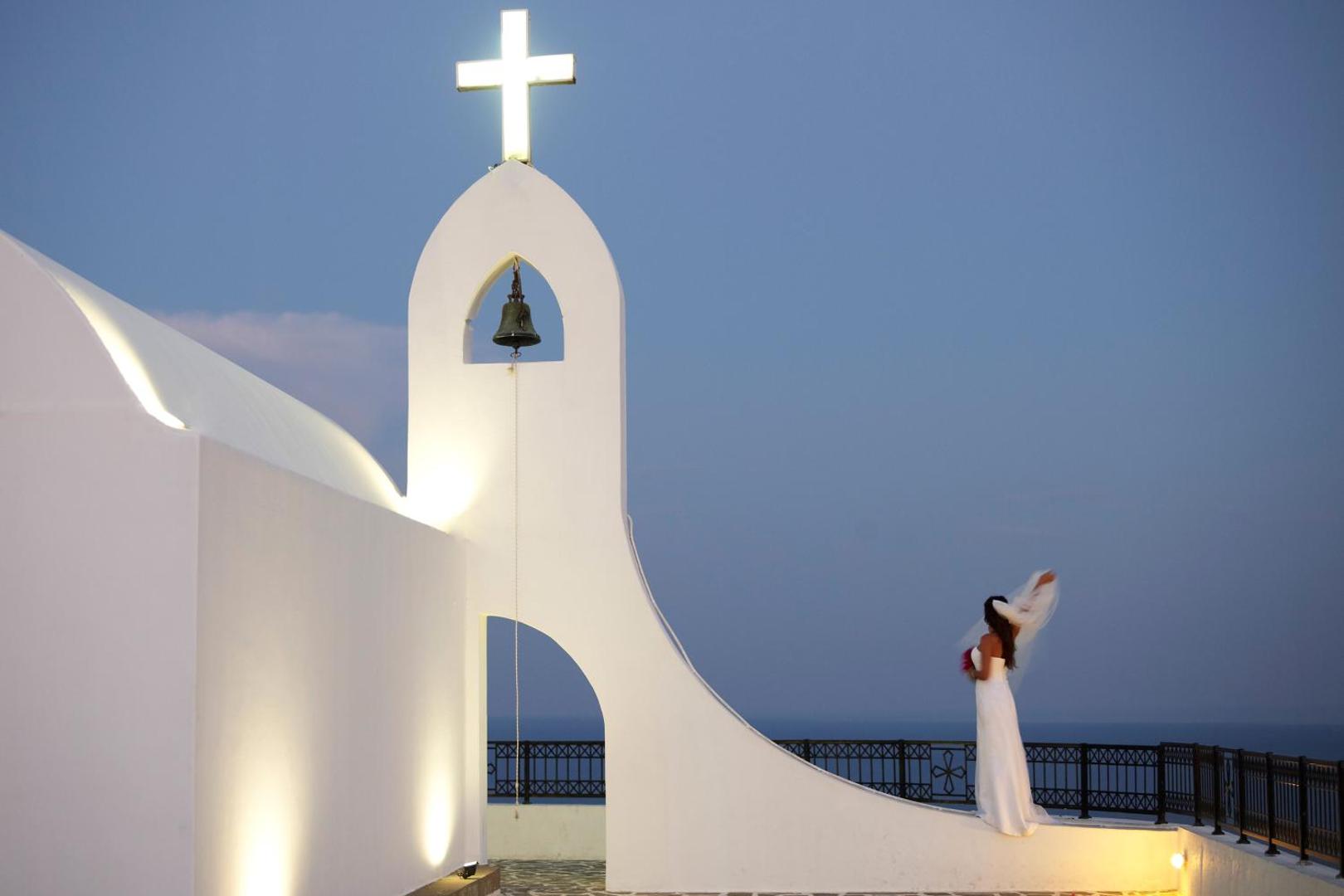 Līgava pie izgaismotas baltas baznīcas zvanu torņa vakara krēslā.