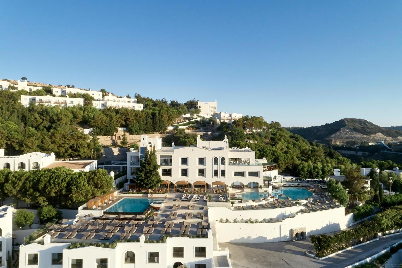 Aerofoto uzņēmums ar Esperos Village Blue & Spa kompleksu un baseiniem kalna nogāzē.