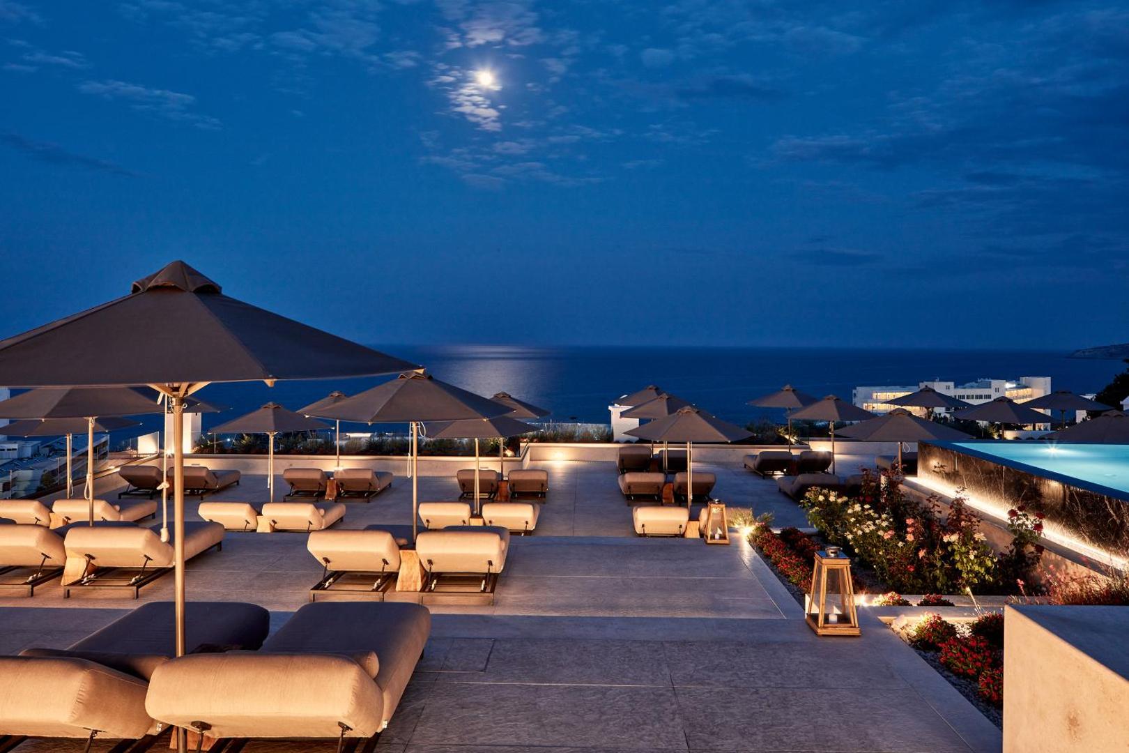 Viesnīcas terase ar zviļņiem un baseinu nakts laikā mēness gaismā.