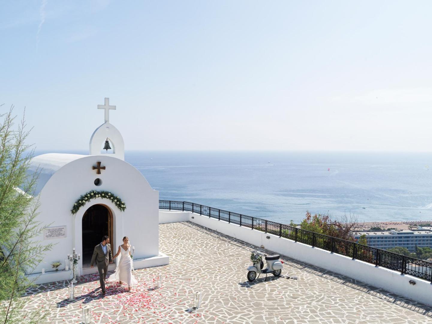 Jaunlaulātie pie baltas baznīcas piekrastē ar skatu uz jūru.