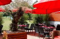 Hôtel Restaurant Le Colibri في Douvrin: فناء به طاولات ومظلات حمراء وشجرة