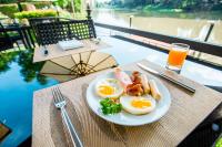 Een bord met eieren en spek op tafel, met een glas sinaasappelsap erbij. bij Aruntara Riverside Boutique Hotel in Chiang Mai