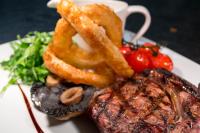 Un plato de comida con bistec, aros de cebolla y verduras. en The White Hart Hotel, en Moretonhampstead