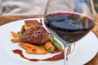 een bord vlees en groenten met een glas wijn bij Hotel Babylon Heerhugowaard - Alkmaar in Heerhugowaard