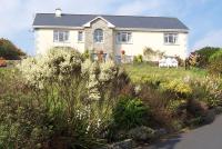 a white house with flowers in front of a yard at Buttermilk Lodge in Clifden
