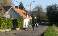 two people riding bikes down a street next to a house at La Quitapenas in Ronse