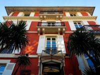 ein hohes rotes Gebäude mit Palmen davor in der Unterkunft Hôtel &amp; Espace Bien-être La Maison du Lierre in Biarritz