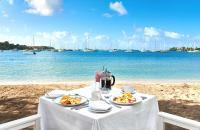 a table with two plates of food on a beach at Calabash Hotel in Saint Georgeʼs