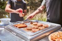 a man cooking food on a grill with sausage and donuts at Lorne Foreshore Caravan Park in Lorne