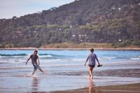 two people walking in the water on a beach at Lorne Foreshore Caravan Park in Lorne