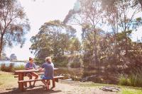 two people sitting on a picnic table by a lake at Lorne Foreshore Caravan Park in Lorne