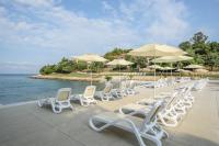 eine Reihe von weißen Stühlen und Sonnenschirmen neben dem Wasser in der Unterkunft Maistra Select Petalon Resort in Vrsar