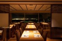 Un restaurante con largas mesas y sillas y vista a la ciudad. en HOTEL MYSTAYS PREMIER Narita, en Narita