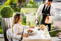 卡利亚里撒丁岛套房和餐厅酒店的一名男子正在餐桌上给一名女子倒一盘食物。