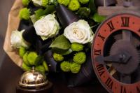 a clock next to a bouquet of white roses at Magus Hotel in Baia Mare