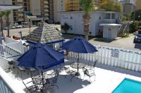 3 Tische und Stühle mit Sonnenschirmen neben einem Pool in der Unterkunft Edgewater Inn in Myrtle Beach