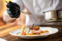 Un chef sostiene una cuchara sobre un plato de comida. en Hotel im Park, en Bad Radkersburg