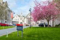 un cartel en la hierba junto a un árbol con flores rosas en The Management Centre, en Bangor