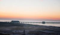 einen Strand mit einem Pier im Wasser bei Sonnenuntergang in der Unterkunft Grand Beach Resort Penthouse 1 in Gulf Shores