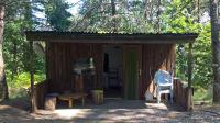 a cabin in the woods with a bench and a chair at La Ptite Ferme de Caro in Meyrignac-lʼÉglise