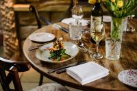 a wooden table with a plate of food and glasses of wine at Le Petit Chateau & William de Percy in Otterburn