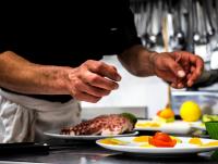 un uomo che prepara il cibo in una cucina con piatti di cibo di Hotel Continental a Pietra Ligure