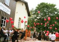 a group of people sitting outside of a building with red balloons at Hotel Zur Fernmühle in Ziegenrück