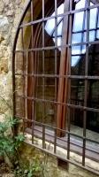 a window with bars on a stone building at Au coeur de Beynac, une maison de caractère avec jardin terrasse in Beynac-et-Cazenac