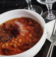 a bowl of food with beans and meat on a table at Hotel Echaurren Relais & Châteaux in Ezcaray