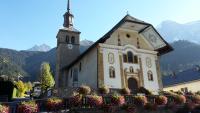 a church with a clock tower and flowers in front of it at Le Lièvre Blanc, appartement N°2 in Les Contamines-Montjoie
