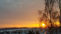 a sunset over a snowy field with the sun in the sky at Villa Jani b&amp;b in Breitscheid
