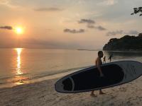a man standing on the beach holding a surfboard at Sarikantang Resort & Spa, Koh Phangan in Haad Rin