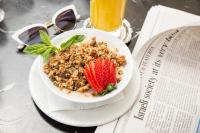 Un tazón de granola y una fresa en un plato junto a un periódico. en Cucu Hotel, en Tel Aviv