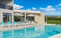 a swimming pool with chairs and umbrellas next to a house at Contemporary Villa Nada with Pool and Sauna in Tinjan