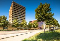 a tall building next to a street with a tree at Airport Hotel Basel - Convenient &amp; Friendly in Basel