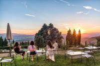 een groep mensen die aan tafels in het gras zitten met de zonsondergang bij Villa Pitiana in Donnini