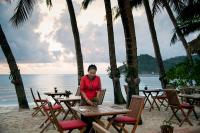 a woman sitting at a table with a laptop on the beach at Anantara Rasananda Koh Phangan Villas in Thong Nai Pan Noi