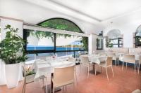 Un restaurante con mesas y sillas blancas y grandes ventanales. en Il Cefalo Hotel & Restaurant, en Castellabate
