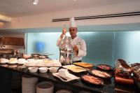 a chef standing in a kitchen with a bottle of food at Gloria Hotel Amman in Amman