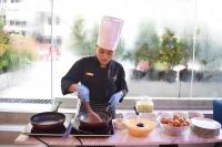 Un chef cocinando comida en una sartén sobre un mostrador. en Aspira One Sutthisan, en Bangkok