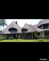 two people standing in front of a house with a thatched roof at Diani Beach-Villa Kirsch in Galu