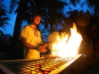 um homem parado em frente a uma grelha com fogo em Tempat Senang Spa Resort & Restaurant em Sekupang
