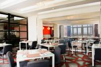 un restaurante con mesas, sillas y ventanas blancas en Onomo Hotel Dar es Salaam, en Dar es Salaam