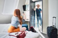 a woman sitting on a bed looking at a man in a mirror at WIROtel Warnemünde in Warnemünde