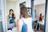 a woman is looking at her reflection in a bathroom mirror at WIROtel Warnemünde in Warnemünde