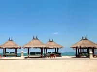 a group of picnic tables and straw umbrellas on a beach at Novotel Lombok Resort & Villas in Kuta Lombok