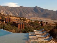 a pool with lounge chairs and mountains in the background at Encuentro Guadalupe in Valle de Guadalupe