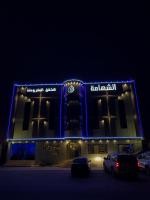 un edificio iluminado con coches estacionados en un estacionamiento en Buyutat Najran Serviced Apartments بيوتات نجران للشقق المخدومة, en Najrán