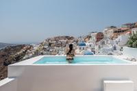 a woman sitting on the edge of a pool overlooking a city at Aspaki by Art Maisons in Oia